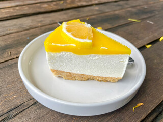 Close-up of a fresh lemon cheesecake slice with biscuit base on a white plate over wooden table