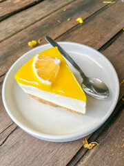 Close-up of a fresh lemon cheesecake slice with biscuit base on a white plate over wooden table