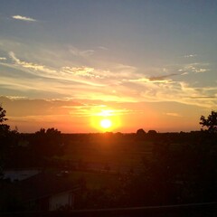 Naklejka premium Sunset over a flat landscape, silhouetting trees and houses