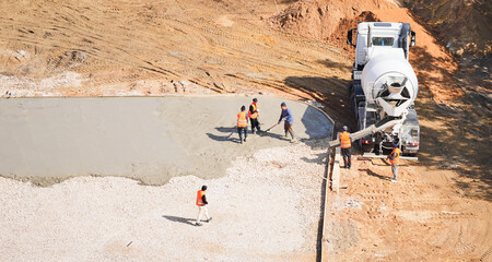 Aerial view of construction workers spreading and leveling fresh concrete from cement mixer truck at building site
