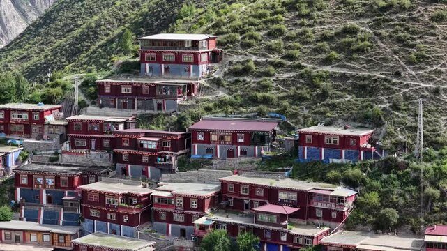 Aerial view of the Dege Parkhang Printing house, a cluster of maroon and white buildings nestled on a green hillside, Sichuan, China.