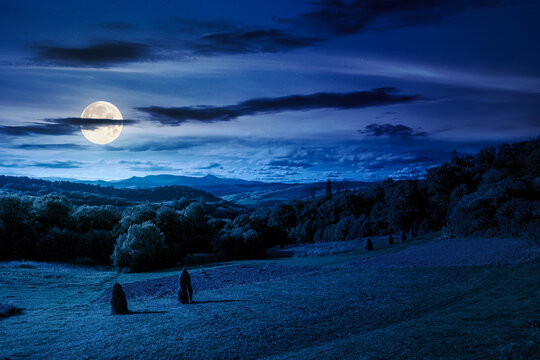 countryside landscape on september night. village in the valley and rural fields on the forested hills in full moon light. mountain ridge with high peak in the distance