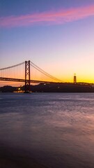 Obraz premium Sunset hues paint the sky over a suspension bridge spanning a calm river