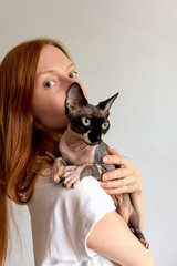 Woman hugging her sphynx cat in a close-up, light background