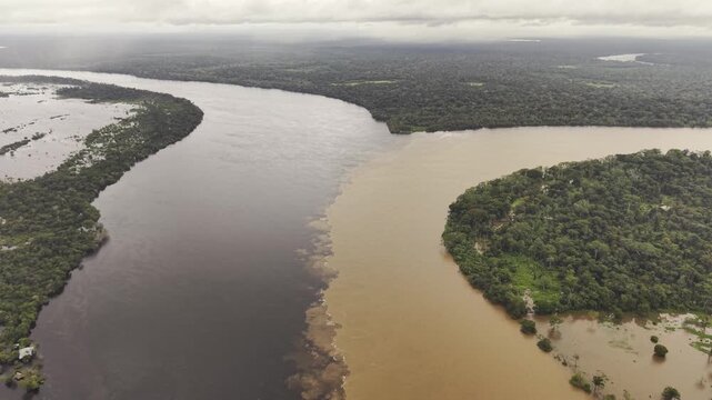 Aerial view of two contrasting rivers joining, showcasing a striking difference in color and texture amidst the lush greenery, Estrella fluvial, Colombia.