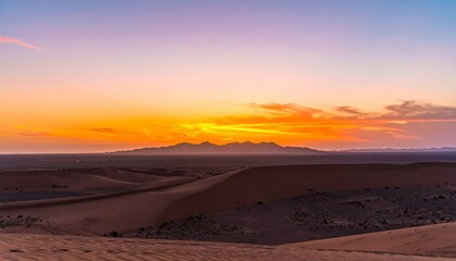 Naklejka premium Vibrant sunset hues paint the sky above a vast, undulating desert landscape, with distant mountains silhouetted against the fiery horizon