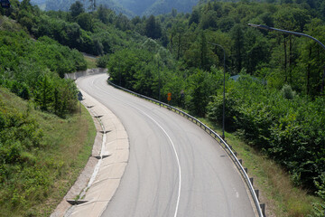 Curved asphalt highway with guardrails and vegetation. Winding mountain road through green forest. Alpine transport route. Empty road with no traffic