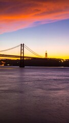 Obraz premium Vibrant sunset hues illuminate a suspension bridge and cityscape across a calm river