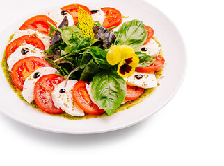 Fresh caprese salad with basil, tomatoes, and mozzarella on a white plate