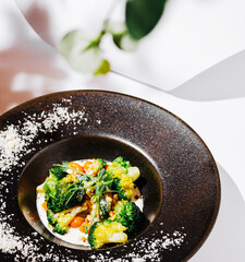 A vibrant dish featuring broccoli, colorful vegetables, and a sprinkle of seasoning is presented in a sleek black bowl