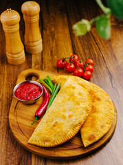 Freshly baked calzones served with sauce and vegetables on a wooden board