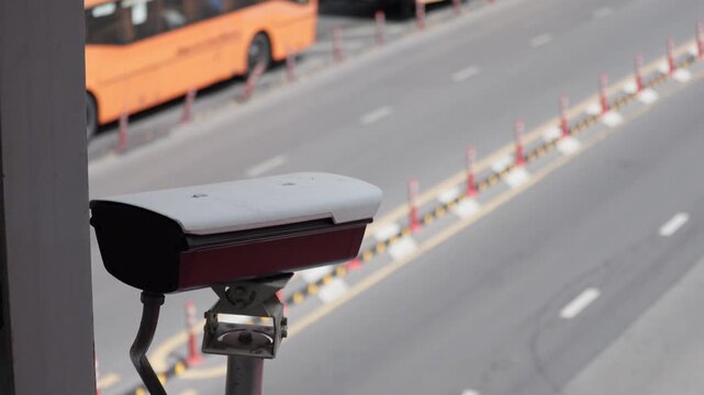 Urban traffic surveillance camera captures vehicle movement at a busy intersection. Featured vehicles include buses, cars, and trucks amidst city infrastructure and road barriers