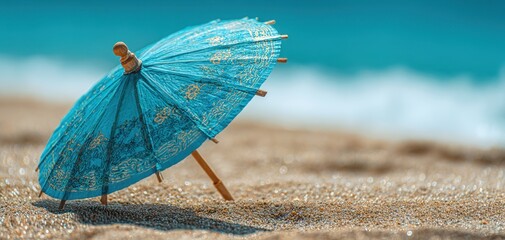 The vibrant beaded blue umbrella resting on sandy beach by the ocean.