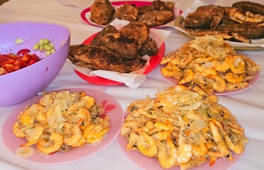 Seafood cuisine of fried Nile tilapia fishes Oreochromis Niloticus fried in deep oil fryer, unpeeled grey shrimps cooked on hot steam and grilled with slices of onion, garlic cumin, and green salad