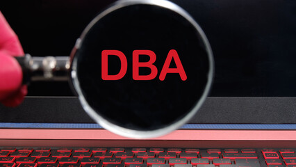 DBA text on the laptop screen through a magnifying glass on a black background. DataBase Administrator or doing business as abbreviation DBA concept