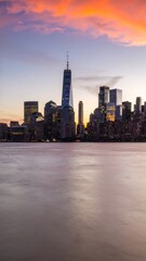 Obraz premium Vibrant sunset hues paint the sky above a city skyline reflected in calm water (1)