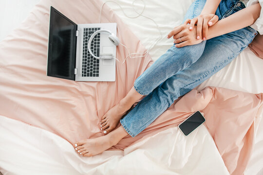 Relaxed remote work setup with laptop, headphones, and smartphone on bed