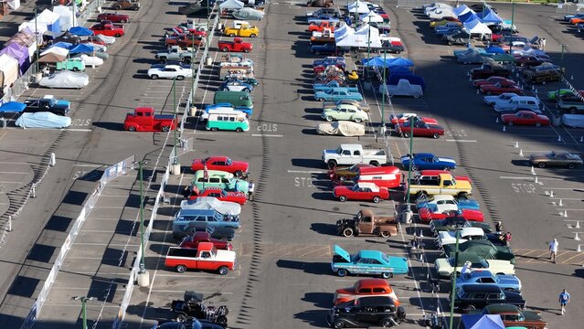 Reno, United States - 08 August 2025: Aerial view of a classic car show in a parking lot, bathed in sunlight, displaying a vibrant tapestry of colors and gleaming chrome under protective canopies.