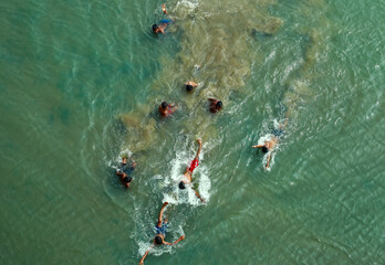 Rangpur, Bangladesh - 30 November 2019: Aerial view of children splashing and swimming in the murky green waters, their dark figures contrasting against the lighter hues of the river.