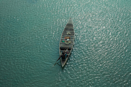 Rangpur, Bangladesh - 30 November 2019: Aerial view of a small wooden boat cutting through the shimmering turquoise waters, its wake a delicate contrast against the expansive aquatic canvas.