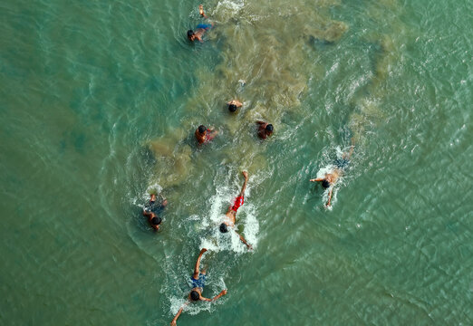 Rangpur, Bangladesh - 30 November 2019: Aerial view of children splashing and swimming in the murky green waters, their dark figures contrasting against the lighter hues of the river.