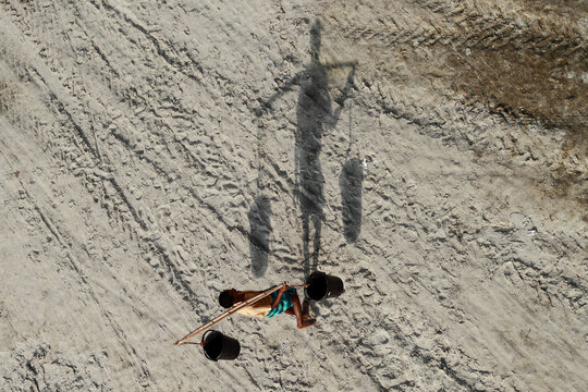 Rangpur, Bangladesh - 01 December 2019: Aerial view of a figure lying on the parched earth, casting a long shadow with buckets in a desolate landscape.