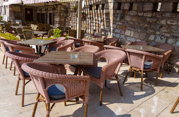 cozy outdoor cafe or restaurant located on embankment of Petrovac city, Montenegro, tables and chairs against the background of a stone wall of an old building