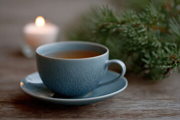Obraz premium Blue teacup on saucer with lit candle and pine branch nearby