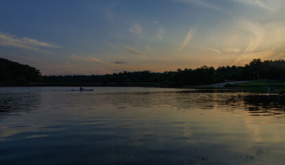 Peaceful sunset over a calm lake with soft reflections of clouds and trees, warm light on the horizon, and a serene evening atmosphere perfect for a tranquil nature scene.