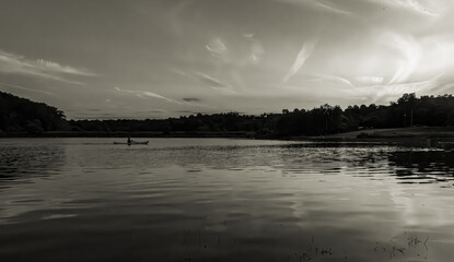 Monochrome sunset over a calm lake with gentle ripples reflecting the sky, distant trees along the horizon, and soft cloud formations creating a peaceful, timeless landscape.