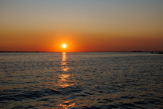 Vibrant sunset over calm ocean waters, casting a golden reflection across the waves under a warm orange and red sky, creating a peaceful and serene coastal evening scene.
