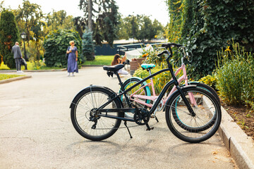 Fototapeta premium bicycles parked in a row at an outdoor bike rack under lush green trees in a sunny park setting. Ideal image for eco-friendly transport and lifestyle concepts.