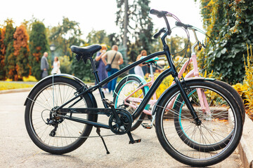 Fototapeta premium bicycles parked in a row at an outdoor bike rack under lush green trees in a sunny park setting. Ideal image for eco-friendly transport and lifestyle concepts.
