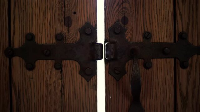 A close-up on aged metal hinges and wooden textures as an old rustic door slowly creaks open to reveal warm interior lighting