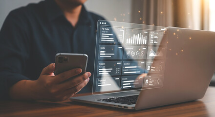 Person using smartphone with laptop displaying data visualization on a wooden table indoors setup
