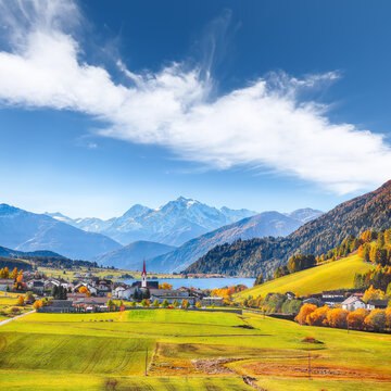 Fabulous autumn view of St.Valentin village and Haidersee (Lago della Muta) lake with Ortler peak on background.