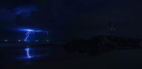 View of electrifying lightning illuminating the dark ocean waters near a lifeguard tower under the moody sky, Redhead Beach, Newcastle, Australia.