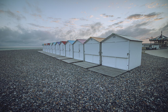 View of a line of colorful beach huts standing proudly on a shingle beach under a moody sky where the sea meets the land, Le TrÃ©port, Normandy, France.