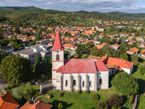 Aerial view of a church with a striking red roof stands prominently amidst the town's landscape, surrounded by lush greenery, Banska Bela, Slovakia.