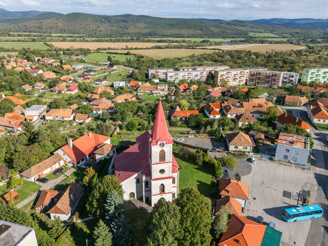 Aerial view of a red-roofed church steeple piercing the skyline amidst a tapestry of homes and green trees, Ko&Aring;&iexcl;ice Region, Slovakia.