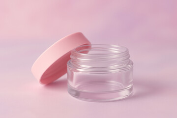 A clear, empty glass jar with a pale pink lid sits slightly ajar on a pink background.