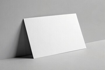 Blank white card leaning against a grey wall paper