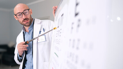 A handsome, slightly unshaven man in glasses and a white lab coat performs a vision check on a...