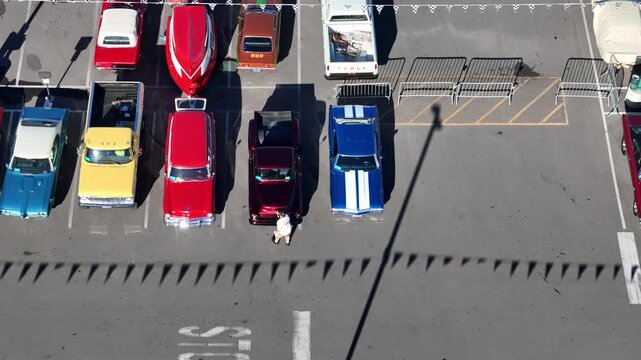 Reno, United States - 08 August 2025: Aerial view of classic cars in a parking lot, their vibrant colors sharply contrasting with the stark grey asphalt.