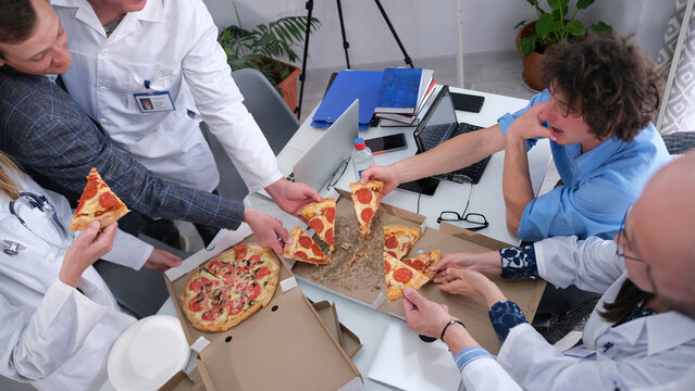 A hungry team of doctors eat delicious hot flavorful pizza together. Lunch break at the clinic. The interns ordered pizza. Hospital staff are eating in the staff room - Powered by Adobe