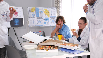 A team of hungry interns and doctors is eating pizza in the staff room. People in white lab coats are having fun at lunch in the hospital office