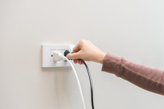 Hand of woman plugged in, unplugged electricity cord cable at home, put on or remove electric plug cable in socket on wall outlet for saving, control power electrical energy, eco environment concept.
