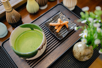 Traditional Japanese tea ceremony setup with matcha green tea in ceramic bowl and traditional sweets on wooden tray reflecting Japanese style and culture in serene setting