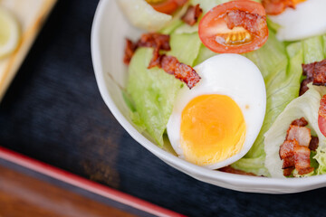 Boiled egg with crispy bacon and fresh tomato on green lettuce in bowl reflects traditional Japanese style and culture in simple and healthy meal presentation