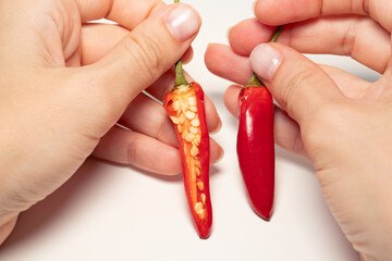 Close-up of hands holding a fresh red chili pepper, one half cut open to reveal seeds, isolated on white background